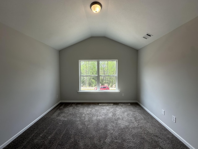 spare room with dark carpet, baseboards, lofted ceiling, and visible vents