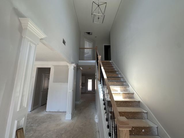 stairs with unfinished concrete flooring, a towering ceiling, visible vents, and ornate columns