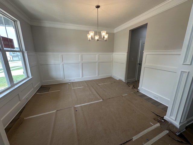 unfurnished dining area featuring a wainscoted wall, ornamental molding, a decorative wall, and an inviting chandelier