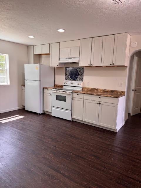 kitchen with dark wood-type flooring, a textured ceiling, under cabinet range hood, and white appliances
