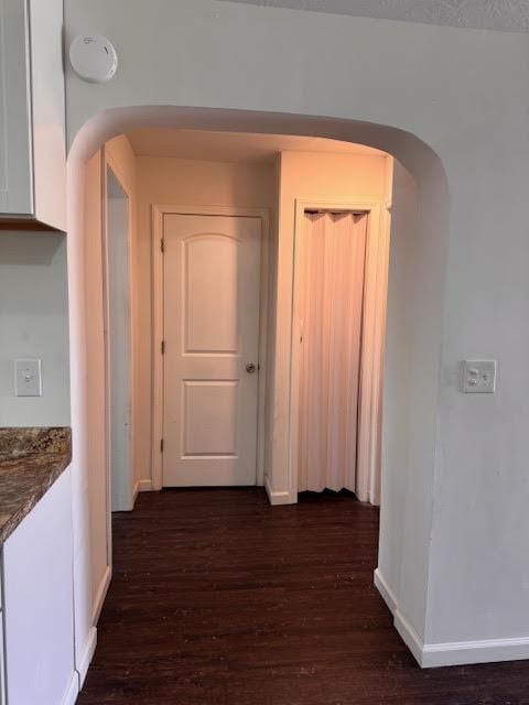 hall with arched walkways, baseboards, and dark wood-style floors