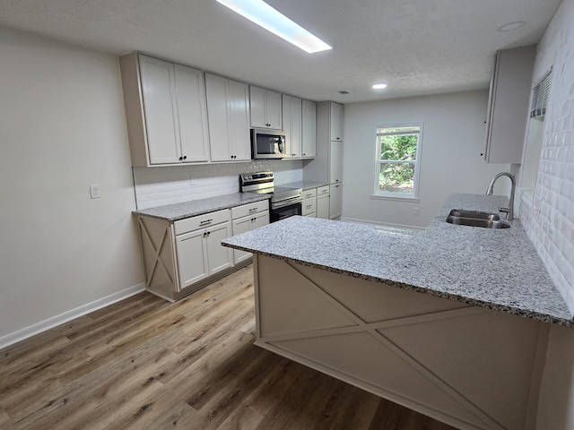 469 Lawrence Dr, Evans, GA 30809 - kitchen featuring appliances with stainless steel finishes, a peninsula, tasteful backsplash, light wood-type flooring, and light stone counters
