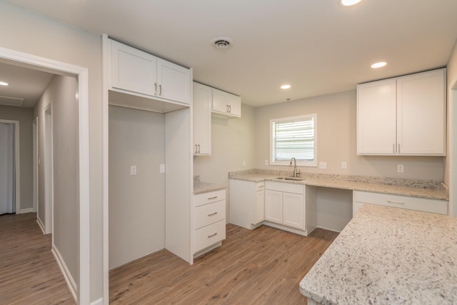 kitchen featuring light stone counters, light hardwood / wood-style floors, white cabinetry, and sink