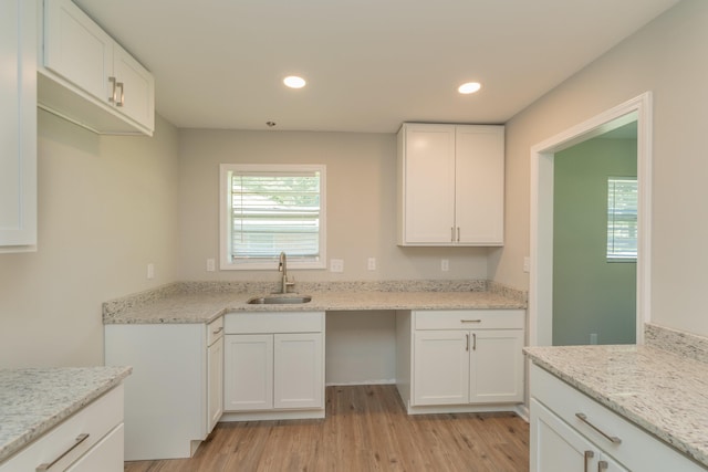 kitchen with light stone counters, sink, white cabinets, and light wood-type flooring