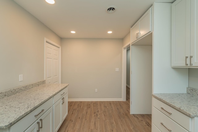 kitchen featuring light stone countertops, light wood-type flooring, and white cabinetry