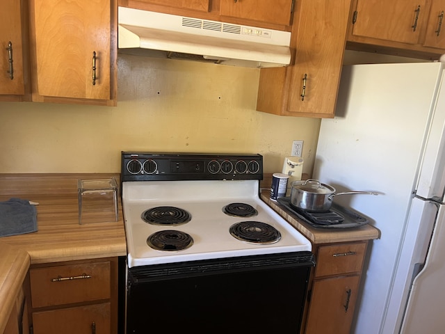303 Spruce St, Louisville, GA 30434 - kitchen with light countertops, under cabinet range hood, range with electric stovetop, freestanding refrigerator, and brown cabinets
