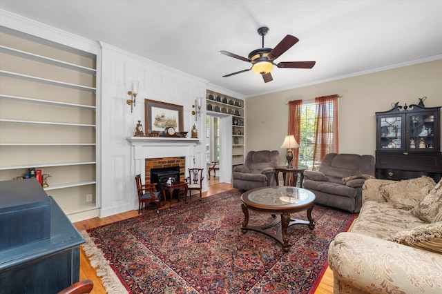 104 Sim St, Washington, GA 30673 - living room featuring crown molding, ceiling fan, built in shelves, wood finished floors, and a brick fireplace
