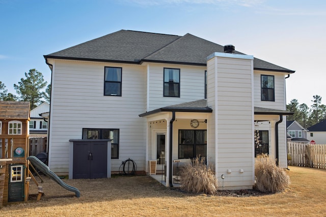 back of property featuring a playground, fence, and a shingled roof