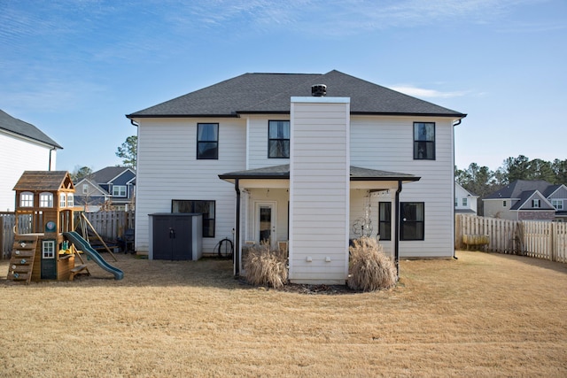 back of house featuring a lawn, a shingled roof, a playground, and fence