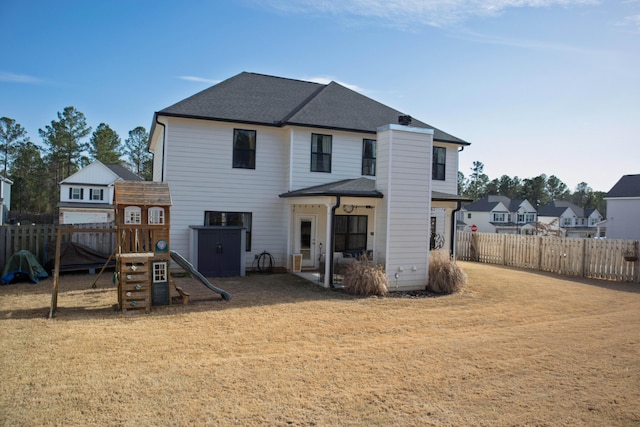 back of house with a fenced backyard, a playground, a yard, roof with shingles, and a patio area