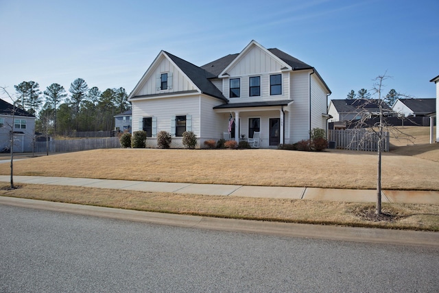 view of front of home with covered porch, board and batten siding, a front yard, and fence