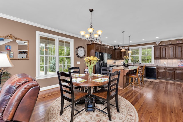 dining area with light wood-type flooring, a notable chandelier, ornamental molding, and sink