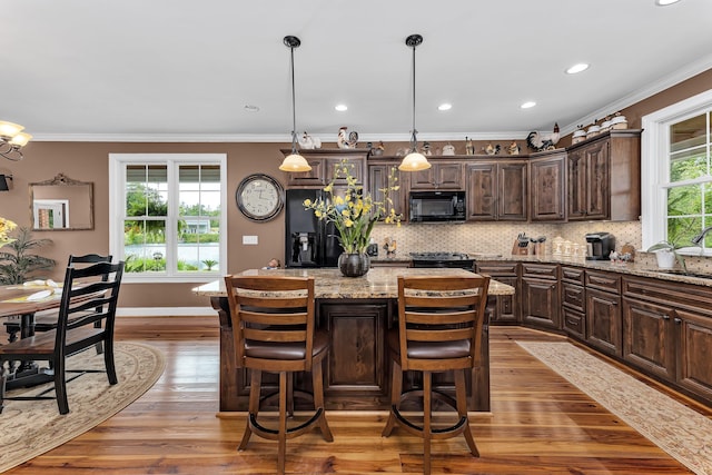 kitchen featuring light stone countertops, dark brown cabinets, black appliances, hardwood / wood-style floors, and a kitchen island