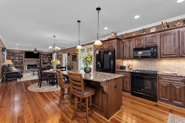 kitchen with black appliances, light stone countertops, ornamental molding, light hardwood / wood-style floors, and a kitchen island