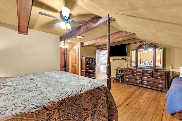 bedroom featuring vaulted ceiling with beams, ceiling fan, light wood-type flooring, and a textured ceiling