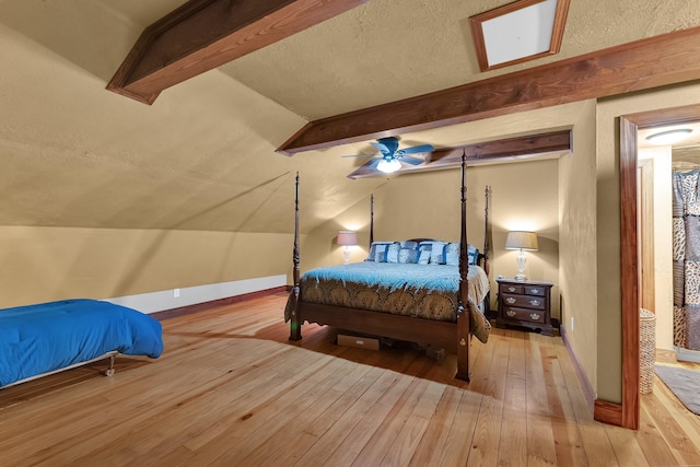 bedroom featuring light wood-type flooring, a textured ceiling, vaulted ceiling with beams, and ceiling fan