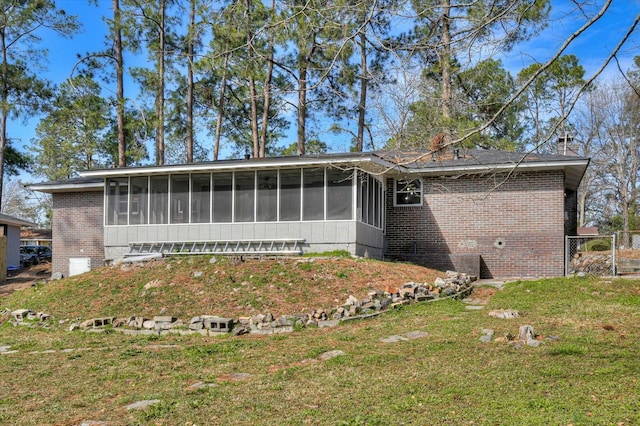 rear view of house featuring a sunroom, a chimney, a lawn, and brick siding