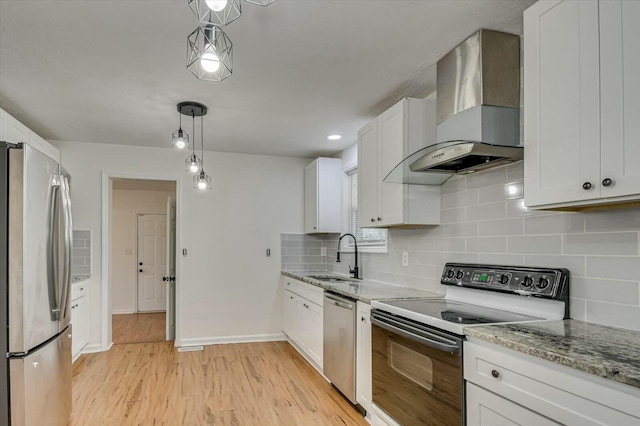 kitchen with white cabinets, light stone counters, stainless steel appliances, wall chimney range hood, and a sink