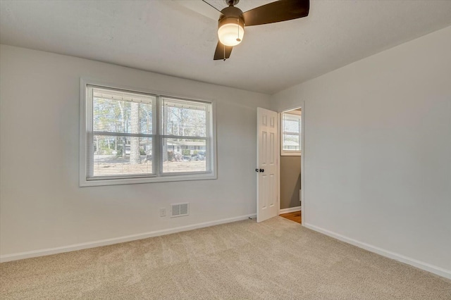 unfurnished room with a ceiling fan, light colored carpet, visible vents, and baseboards