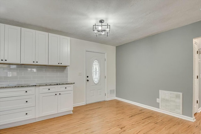 foyer entrance with a textured ceiling, light wood finished floors, visible vents, and baseboards