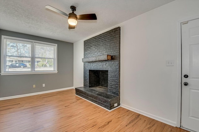 unfurnished living room featuring a fireplace, light wood-style flooring, ceiling fan, a textured ceiling, and baseboards