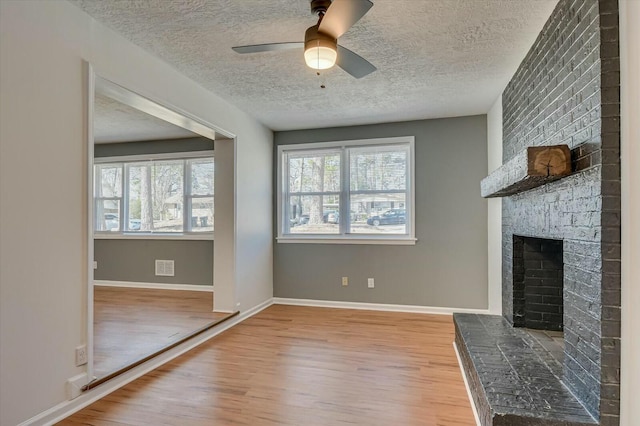 unfurnished living room featuring light wood-style floors, ceiling fan, a fireplace, and a wealth of natural light