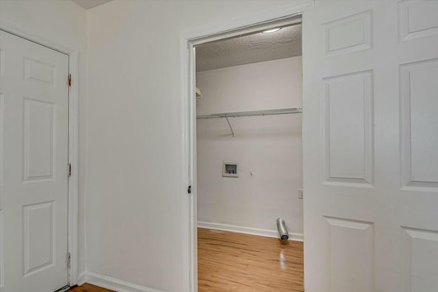 clothes washing area featuring a textured ceiling, laundry area, washer hookup, wood finished floors, and baseboards