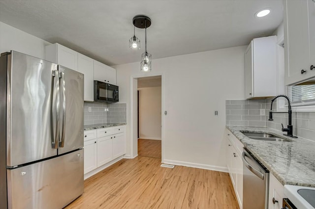 kitchen featuring a sink, white cabinetry, appliances with stainless steel finishes, light stone countertops, and decorative light fixtures