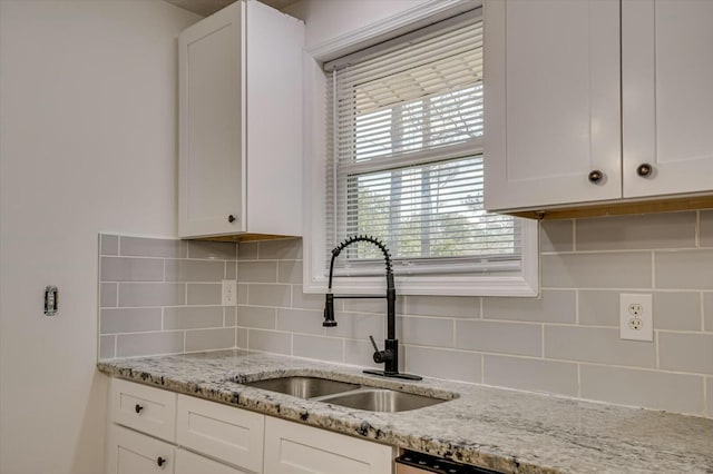 kitchen featuring light stone counters, white cabinets, a sink, and decorative backsplash