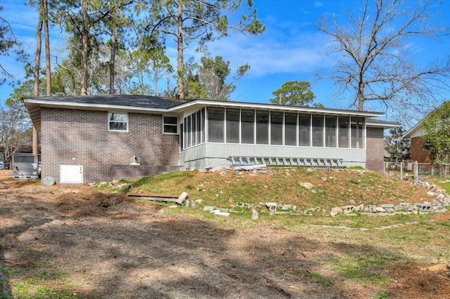 back of property with an attached garage, a sunroom, and brick siding