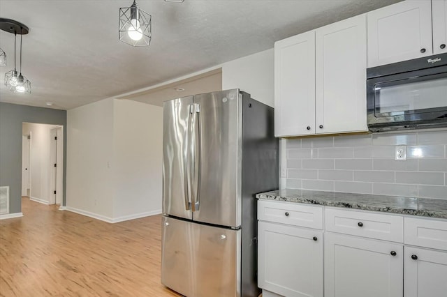 kitchen with light wood finished floors, black microwave, decorative light fixtures, freestanding refrigerator, and white cabinetry