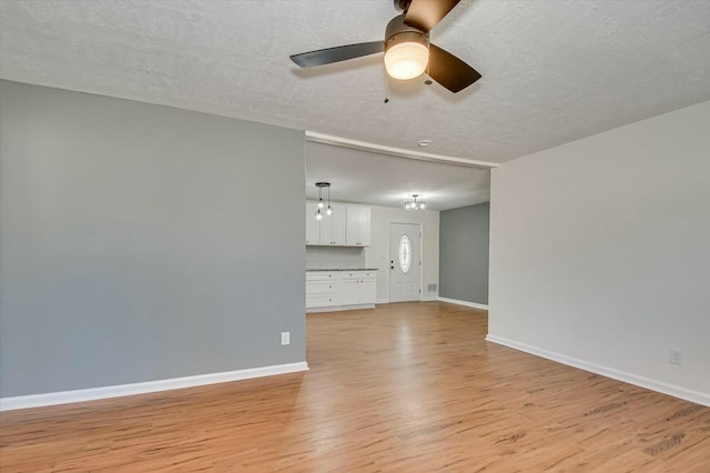 unfurnished living room featuring light wood-type flooring, ceiling fan, baseboards, and a textured ceiling