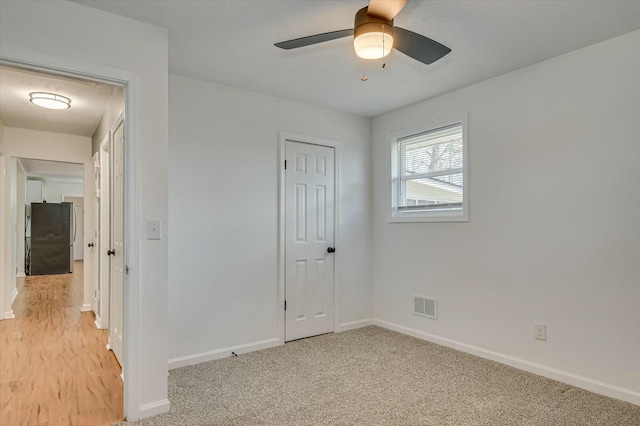 interior space with ceiling fan, light colored carpet, visible vents, baseboards, and freestanding refrigerator