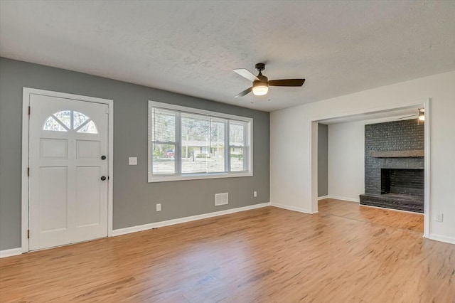 foyer with light wood-style floors, a brick fireplace, a ceiling fan, and a textured ceiling