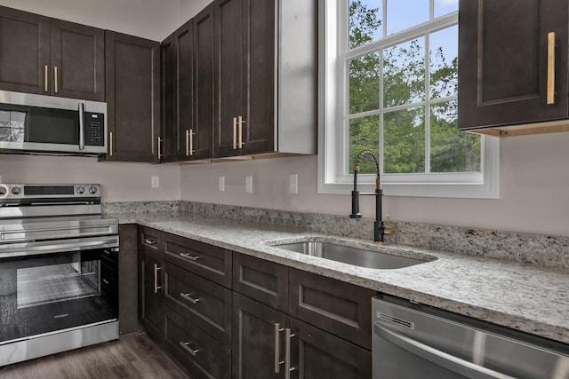 kitchen featuring dark brown cabinetry, stainless steel appliances, light stone counters, and sink