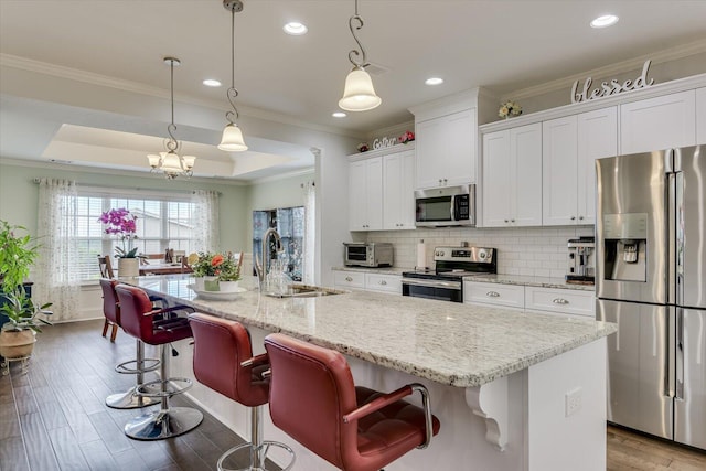 kitchen with appliances with stainless steel finishes, decorative light fixtures, white cabinetry, and a kitchen island with sink