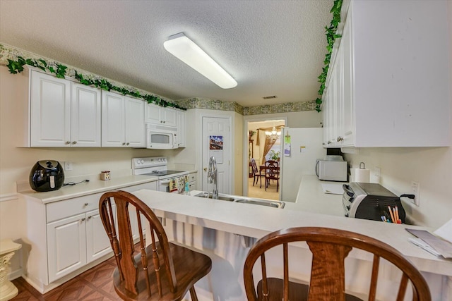 kitchen featuring white appliances, a textured ceiling, white cabinetry, and a sink