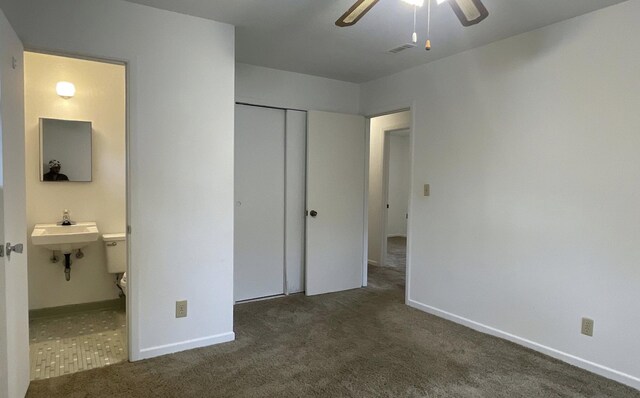 unfurnished bedroom featuring ensuite bath, ceiling fan, a closet, and dark colored carpet