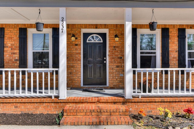 doorway to property with covered porch and brick siding