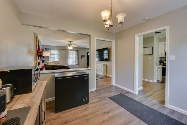 kitchen with ceiling fan with notable chandelier, baseboards, fridge, light wood-type flooring, and stainless steel microwave