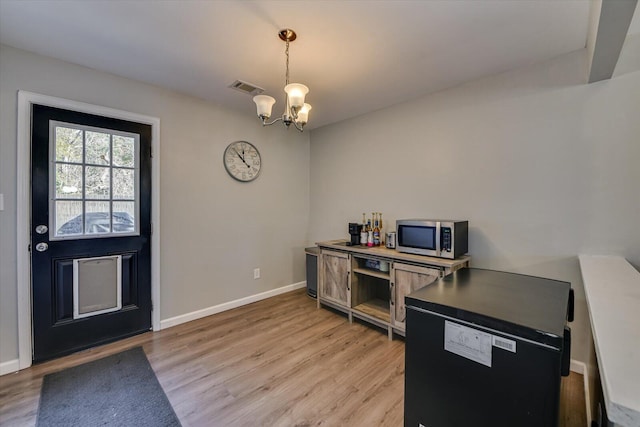 kitchen featuring light wood-style flooring, a notable chandelier, visible vents, baseboards, and stainless steel microwave