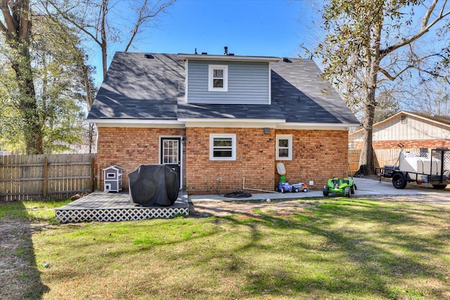 rear view of house with a deck, a yard, brick siding, and a fenced backyard