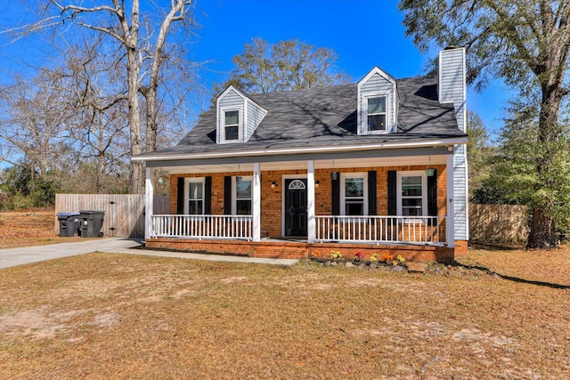 new england style home with a chimney, a porch, fence, a front lawn, and brick siding