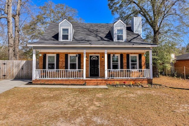 cape cod-style house featuring a chimney, fence, a porch, and brick siding