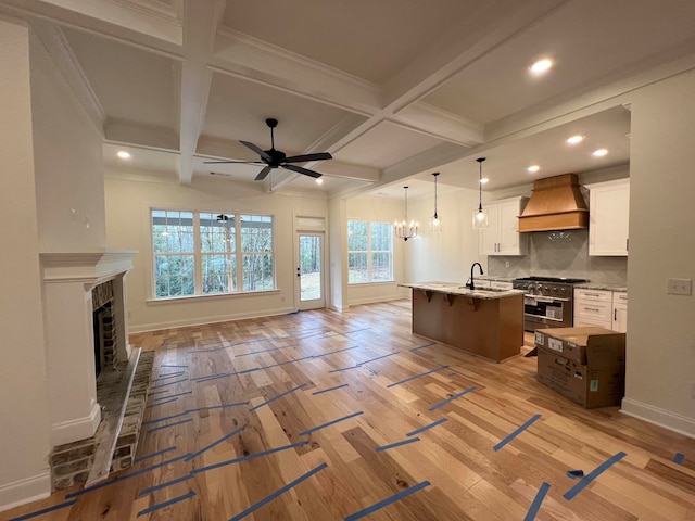 kitchen featuring high end range, premium range hood, a kitchen island with sink, coffered ceiling, and white cabinetry