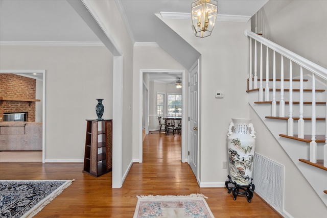 foyer entrance with crown molding, ceiling fan with notable chandelier, hardwood / wood-style floors, and a brick fireplace