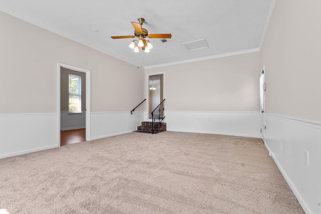 carpeted empty room featuring attic access, baseboards, ceiling fan, and crown molding