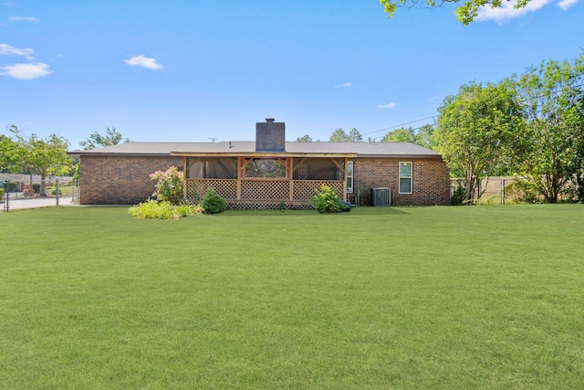 rear view of house with brick siding, a chimney, a sunroom, and a yard