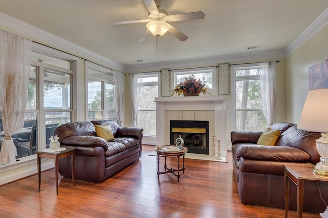 living room featuring ceiling fan, wood-type flooring, ornamental molding, and a tile fireplace