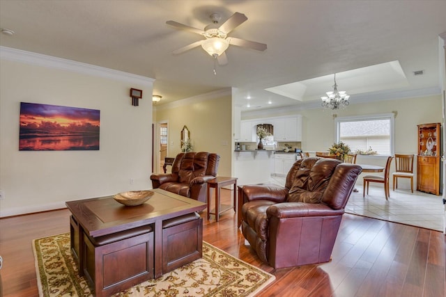 living room featuring ceiling fan with notable chandelier, a tray ceiling, light hardwood / wood-style flooring, and crown molding